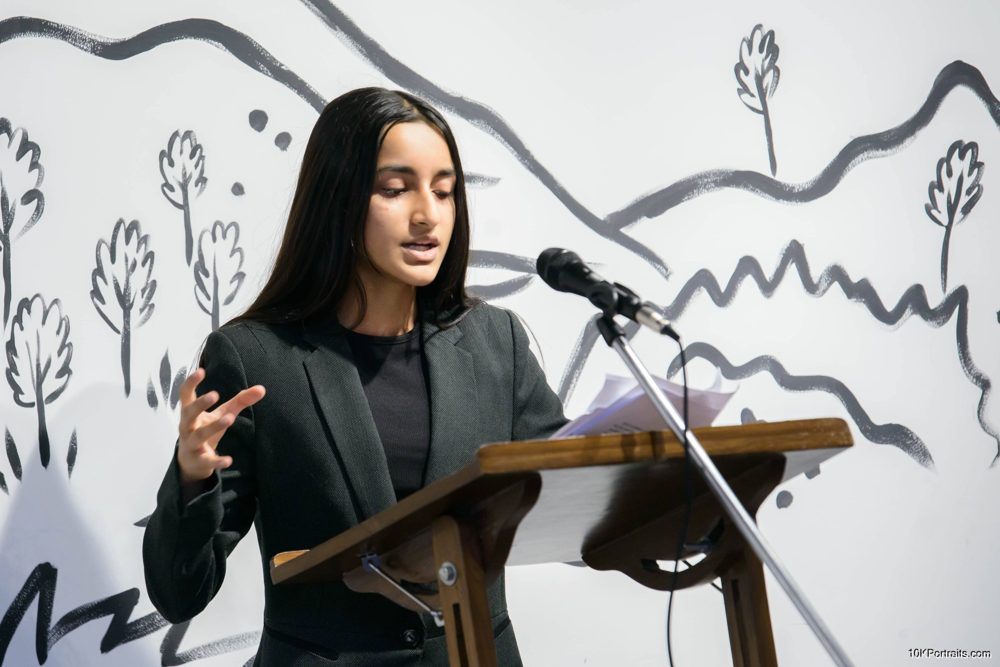 Speaking at a podium with a mountain mural