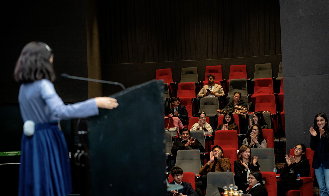 A speaker at the podium with parents and children applauding at the Parent and Child Debate, 2025
