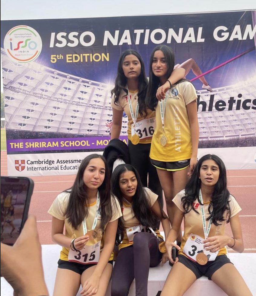 Five athletes in team kit with medals in front of the ISSO National Games banner