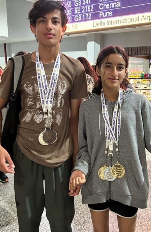 Two athletes wearing ISSO National Games medals at an airport
