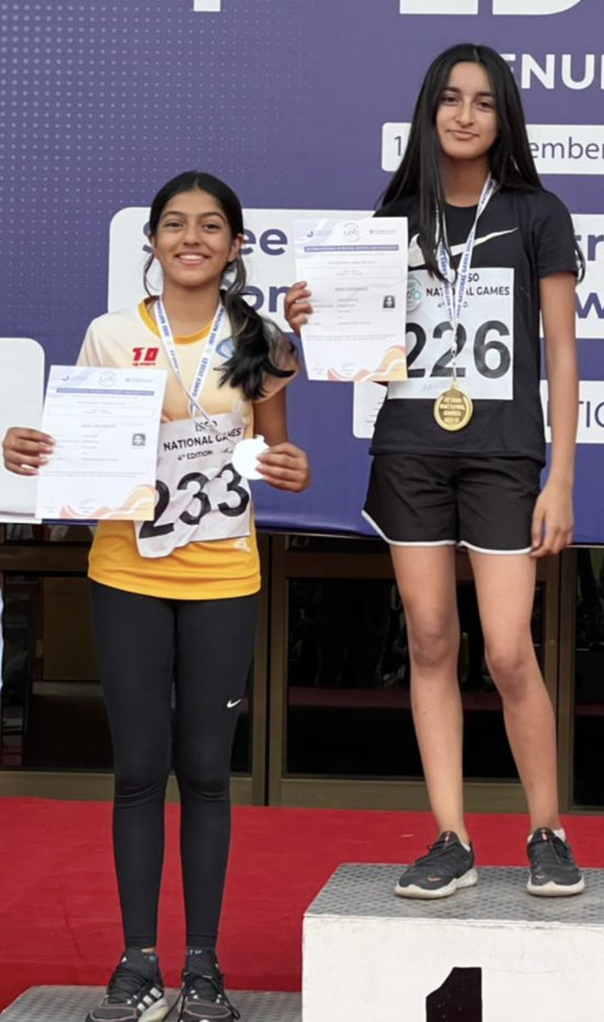 Two athletes on the podium with medals and certificates
